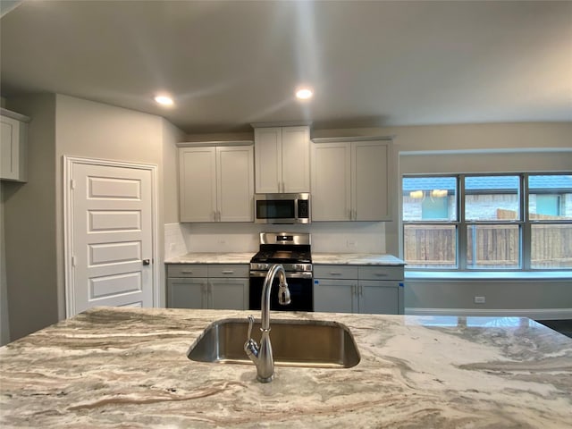 kitchen featuring appliances with stainless steel finishes, light stone countertops, gray cabinets, a sink, and recessed lighting