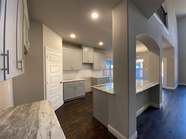 kitchen featuring baseboards, arched walkways, dark wood finished floors, light stone counters, and recessed lighting