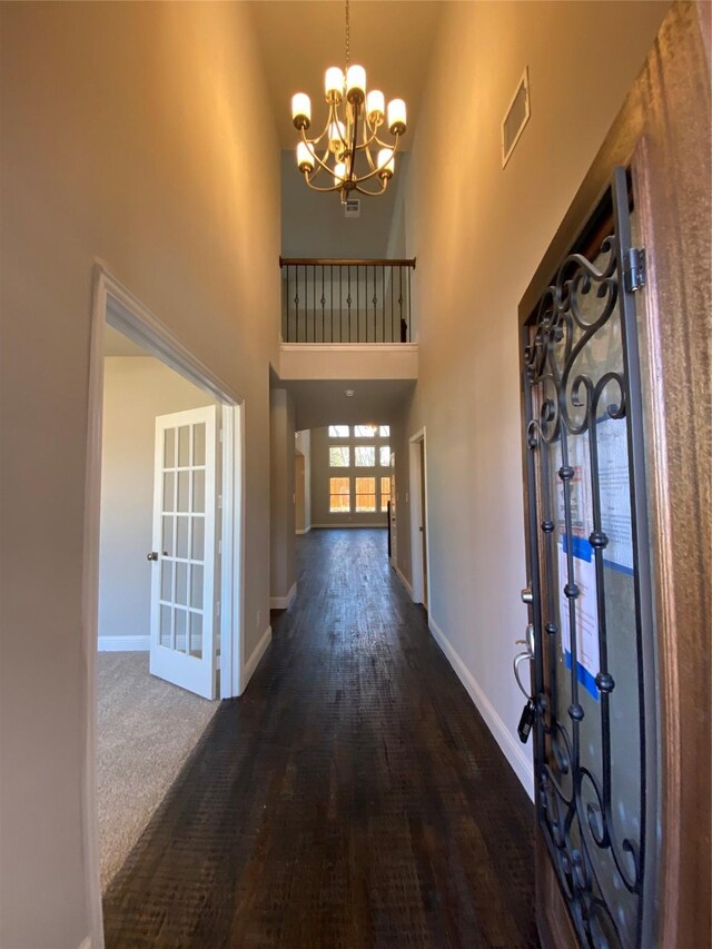 hall with wood-type flooring, a towering ceiling, and a notable chandelier