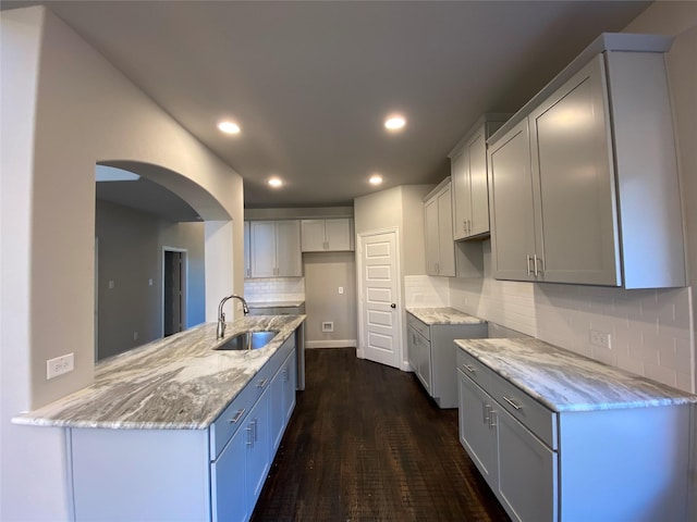 kitchen with dark wood finished floors, recessed lighting, decorative backsplash, a sink, and light stone countertops