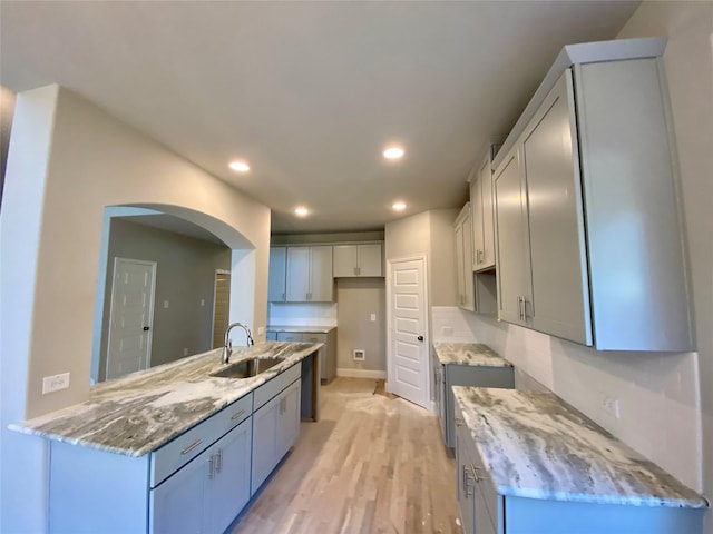 kitchen with light stone counters, sink, gray cabinetry, and light hardwood / wood-style floors