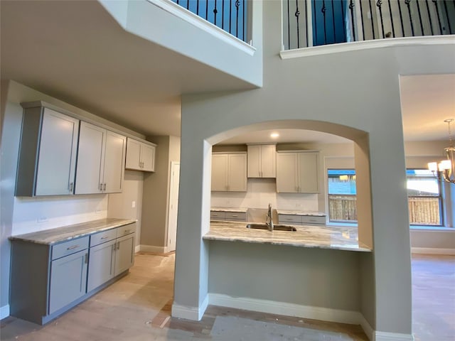 kitchen featuring gray cabinets, sink, a high ceiling, light stone counters, and a chandelier