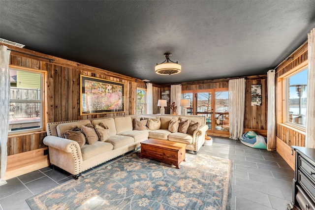 tiled living room featuring a textured ceiling, plenty of natural light, and wood walls