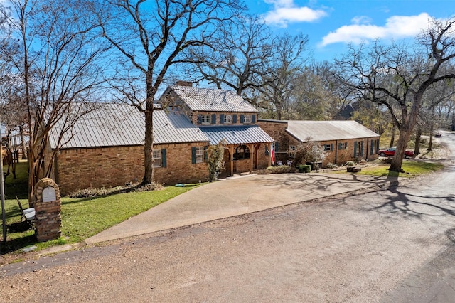 traditional home with a chimney, driveway, brick siding, a front yard, and metal roof
