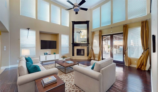 living room with dark wood-type flooring, ornamental molding, a high ceiling, and ceiling fan