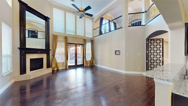 unfurnished living room featuring ceiling fan, a high ceiling, dark hardwood / wood-style flooring, and a healthy amount of sunlight