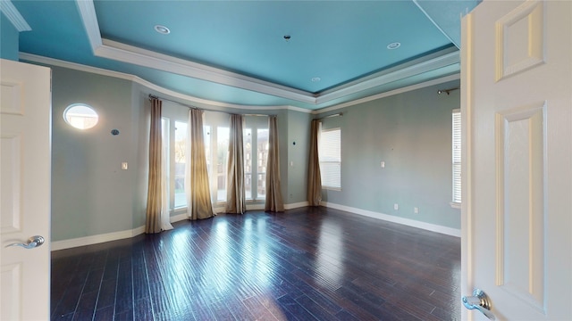 empty room featuring a raised ceiling, dark hardwood / wood-style floors, and ornamental molding