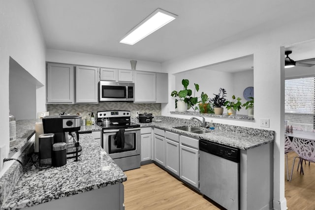 kitchen featuring light hardwood / wood-style floors, gray cabinets, stainless steel appliances, light stone counters, and sink