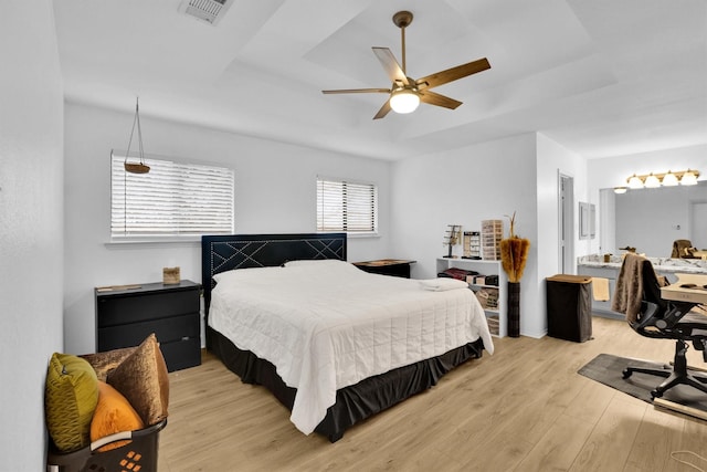 bedroom with a raised ceiling, ceiling fan, and light wood-type flooring