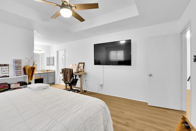 bedroom with a raised ceiling, ceiling fan, light wood-type flooring, and ensuite bathroom