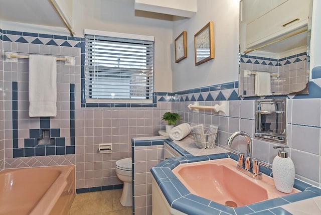 bathroom with tile patterned floors, vanity, a tub, tile walls, and toilet