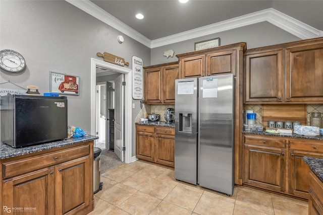 kitchen with dark stone countertops, backsplash, stainless steel fridge with ice dispenser, light tile patterned flooring, and crown molding