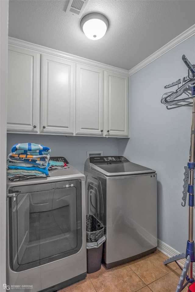 laundry area with light tile patterned floors, washing machine and dryer, a textured ceiling, and cabinets