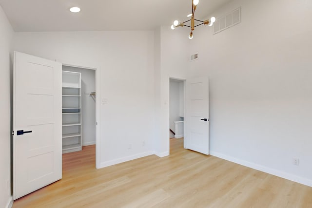 unfurnished bedroom with a walk in closet, a closet, a chandelier, and light hardwood / wood-style flooring