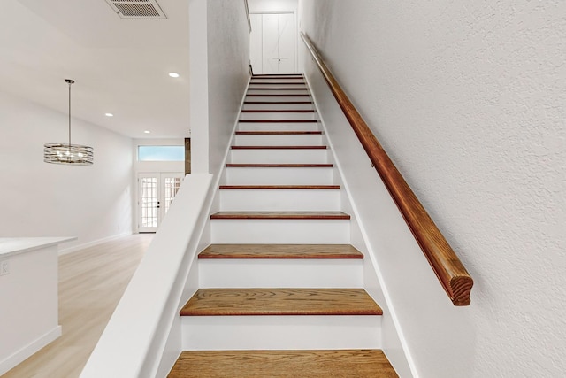 staircase with french doors, a notable chandelier, and hardwood / wood-style flooring