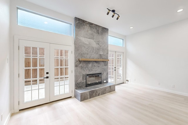 unfurnished living room featuring french doors, a tiled fireplace, and light hardwood / wood-style floors