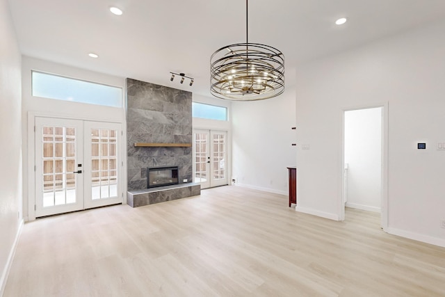 unfurnished living room with light wood-type flooring, a chandelier, french doors, and a tile fireplace