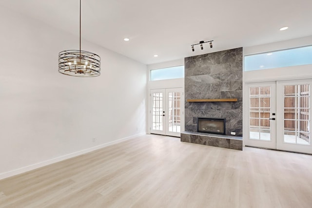 unfurnished living room featuring rail lighting, light hardwood / wood-style floors, french doors, a chandelier, and a tile fireplace