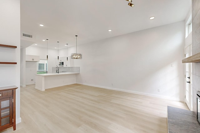 kitchen with decorative light fixtures, light hardwood / wood-style floors, kitchen peninsula, white cabinetry, and a tiled fireplace