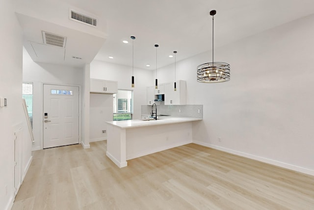 kitchen with pendant lighting, white cabinets, sink, kitchen peninsula, and light wood-type flooring