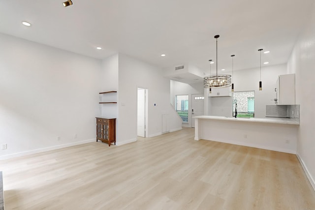 kitchen with decorative light fixtures, white cabinets, kitchen peninsula, and light hardwood / wood-style floors