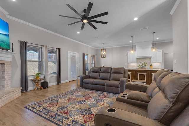 living room featuring ceiling fan with notable chandelier, ornamental molding, a fireplace, and light hardwood / wood-style floors