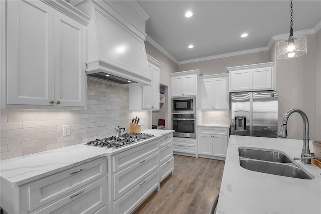 kitchen featuring sink, premium range hood, appliances with stainless steel finishes, white cabinets, and decorative backsplash