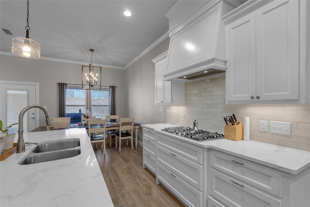 kitchen with sink, white cabinets, hanging light fixtures, stainless steel gas cooktop, and custom range hood