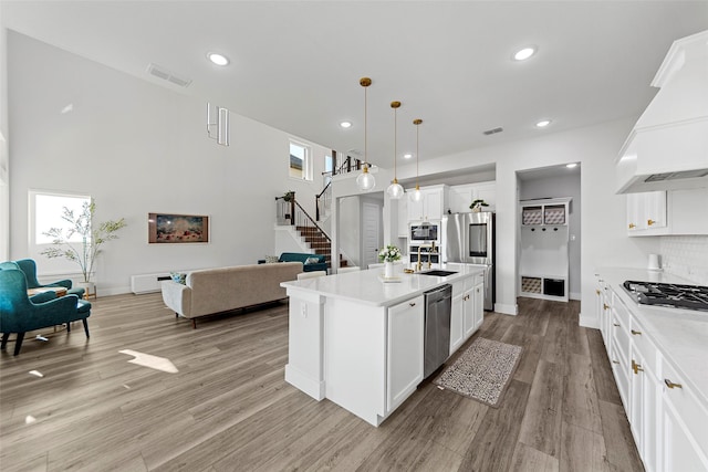 kitchen featuring pendant lighting, custom exhaust hood, an island with sink, stainless steel appliances, and white cabinets