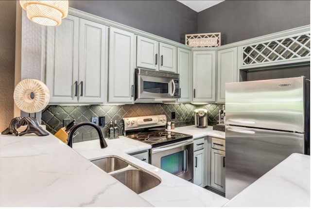 kitchen featuring appliances with stainless steel finishes, decorative backsplash, hanging light fixtures, light stone counters, and sink