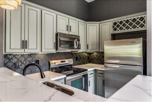 kitchen with light stone counters, sink, backsplash, and appliances with stainless steel finishes