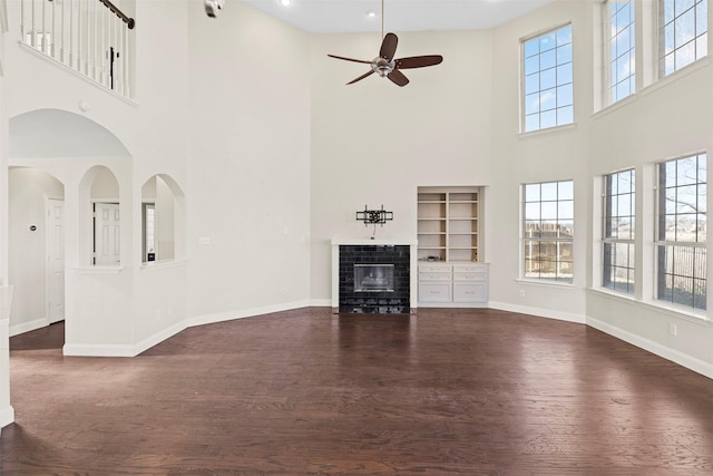 unfurnished living room with dark wood-type flooring, ceiling fan, and a tiled fireplace