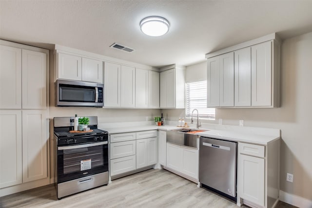 kitchen with a textured ceiling, white cabinets, stainless steel appliances, sink, and light hardwood / wood-style flooring