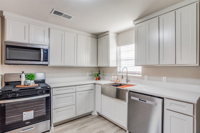 kitchen with stainless steel appliances, light hardwood / wood-style floors, white cabinetry, and sink