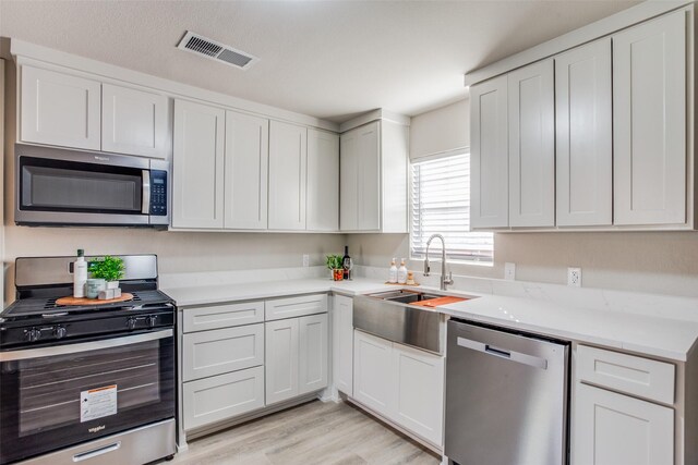 kitchen featuring sink, light wood-type flooring, appliances with stainless steel finishes, a textured ceiling, and white cabinets