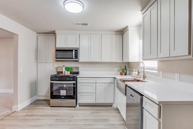 kitchen with white cabinetry, stainless steel appliances, sink, light wood-type flooring, and light stone counters