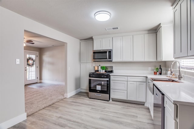 kitchen featuring ceiling fan, sink, light wood-type flooring, stainless steel appliances, and white cabinets