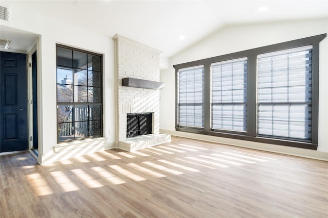 unfurnished living room featuring vaulted ceiling, a fireplace, and light hardwood / wood-style floors