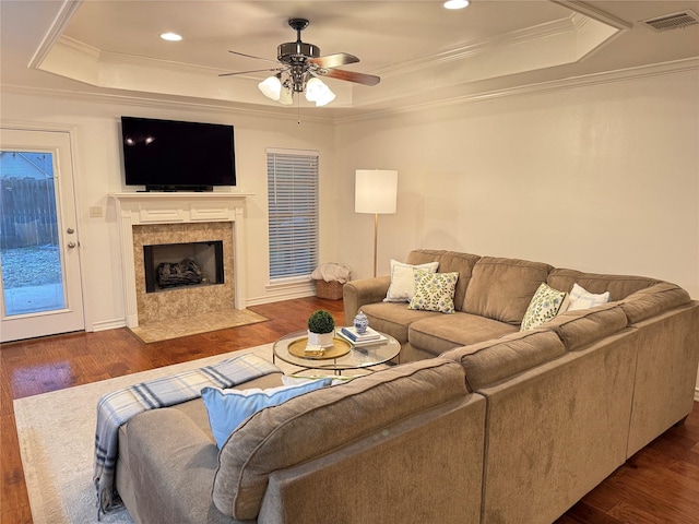 living room with a premium fireplace, ceiling fan, dark hardwood / wood-style flooring, and a raised ceiling