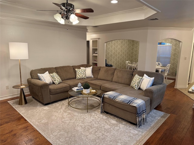 living room with a raised ceiling, ceiling fan, dark wood-type flooring, and ornamental molding