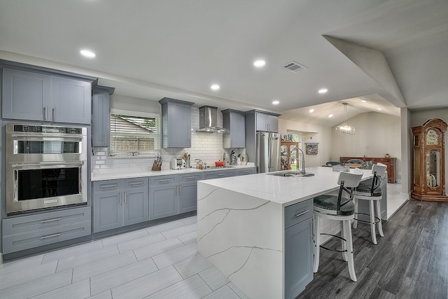 kitchen with a spacious island, vaulted ceiling, wall chimney exhaust hood, a breakfast bar, and sink