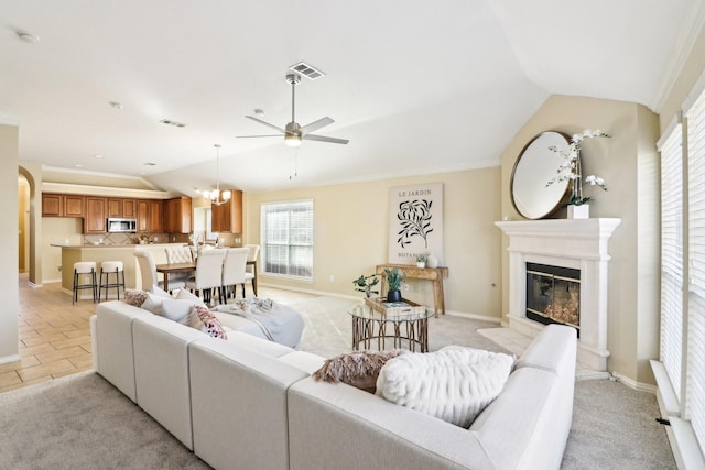 living room with vaulted ceiling, light colored carpet, crown molding, and ceiling fan with notable chandelier