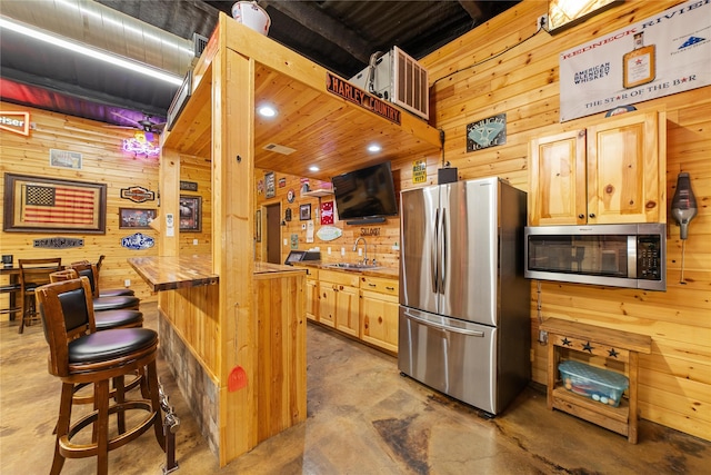 kitchen with light brown cabinetry, butcher block countertops, stainless steel appliances, and wooden walls