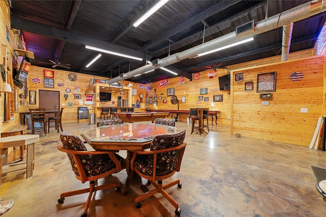 dining area with ceiling fan, concrete flooring, and wood walls