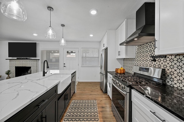 kitchen with white cabinetry, sink, hanging light fixtures, stainless steel appliances, and wall chimney range hood