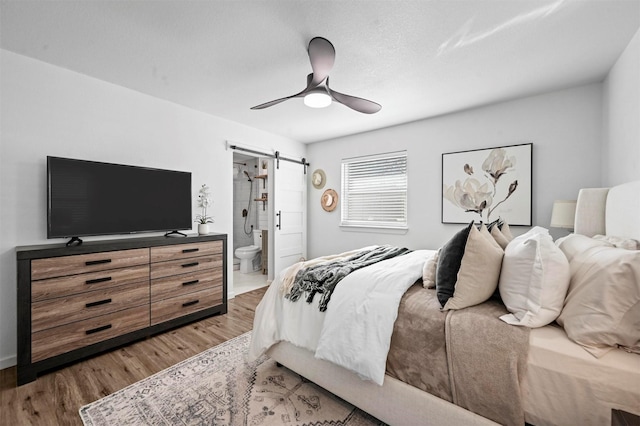 bedroom featuring hardwood / wood-style flooring, ceiling fan, connected bathroom, and a barn door