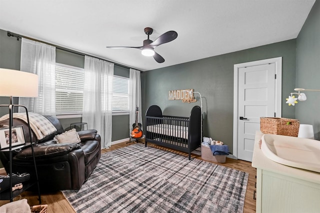 bedroom with a crib, wood-type flooring, sink, and ceiling fan