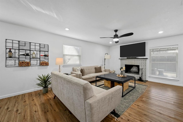 living room featuring a tile fireplace, wood-type flooring, and ceiling fan