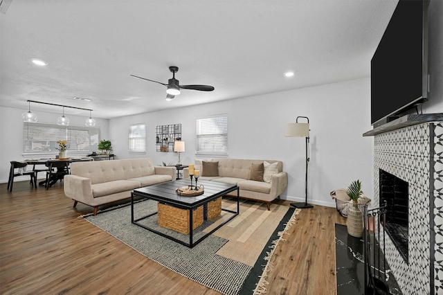 living room with wood-type flooring, a tile fireplace, and ceiling fan