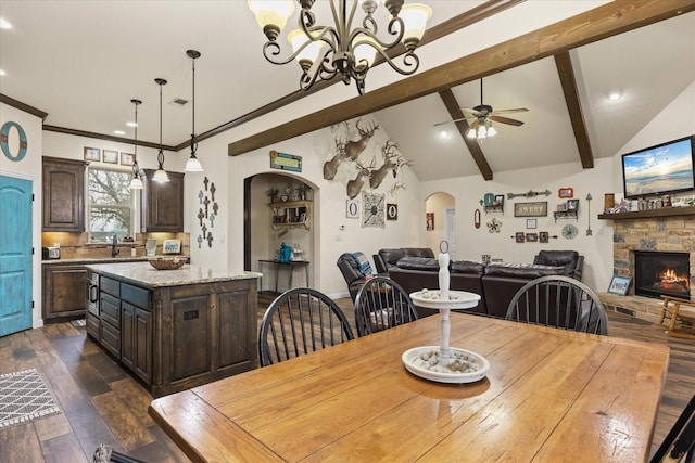 dining area with ceiling fan with notable chandelier, a fireplace, sink, dark hardwood / wood-style floors, and lofted ceiling with beams